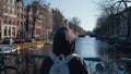 Traveler young girl walks to railing with bicycles on one of bridges of Amsterdam with beautiful view of canal with