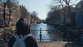 Traveler young girl walks to railing with bicycles on one of bridges of Amsterdam with beautiful view of canal with