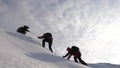 Travelers climb rope to their victory through snow uphill in a strong wind. tourists in winter work together as team