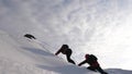 Travelers climb rope to their victory through snow uphill in a strong wind. tourists in winter work together as team