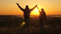 Travelers, a man and a woman with backpack go to edge of mountain in rays of dawn, raise their hands in air and enjoy Royalty Free Stock Photo