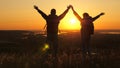 Travelers, a man and a woman with backpack go to edge of mountain in rays of dawn, raise their hands in air and enjoy Royalty Free Stock Photo