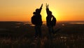 Travelers, a man and a woman with backpack go to edge of mountain in rays of dawn, raise their hands in air and enjoy Royalty Free Stock Photo