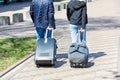 Two people, a man and a woman, walk along the cobbled sidewalk, carrying a travel bag and a suitcase on wheels behind them Royalty Free Stock Photo