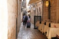 Travelers with suitcases is walking in daylight. Passage between walls to the old town. Summer in Croatia, Dubrovnik.