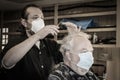 Traveling barber cuts senior mans hair in garage - both wearing masks