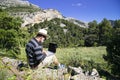 A traveling blogger remotely works on a laptop while enjoying views of the natural mountain landscape outdoors. man working Royalty Free Stock Photo