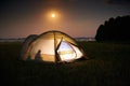 Traveling and camping concept - camp tent at night under a sky full of stars. Orange illuminated tent with a person inside.