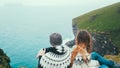 Traveling couple in lopapeysa sweaters sitting on the edge of the cliff and looking at the sea, enjoying the waves. Royalty Free Stock Photo