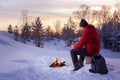 Traveling man in winterwear sitting near fire and having hot drinks.