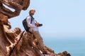 Traveller with camera sits on the edge of a cliff.