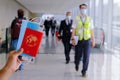 Traveller holding passport, mask, boarding pass in airport. Staff and pilot wearing face masks walking with in background Royalty Free Stock Photo