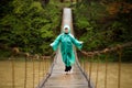 Traveller senior beautiful woman in blue rain jacket cross river by hinged bridge in forest, enjoying silence Royalty Free Stock Photo