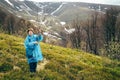 Traveller senior beautiful woman in blue rain jacket and jeans in mountains surrounded by forest, enjoying silence and harmony of