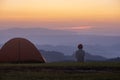 Traveller is sitting by the tent during overnight camping while looking at the beautiful scenic sunset over the mountain for
