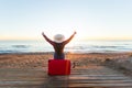 Travelling, holidays and people concept - happy woman sitting on red suitcase in a hat in front of you, watching the sea Royalty Free Stock Photo