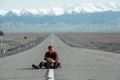 Travelling man sitting in middle of the road with backpack Royalty Free Stock Photo