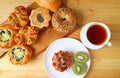 Tray of assorted buns and cut kiwi fruit with hot tea on wooden table Royalty Free Stock Photo