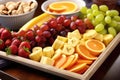 a tray of assorted fresh fruit including oranges, bananas, and grapes