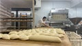 Tray of bread dough cut and ready to bake in the oven and in the background baker spreading the dough on the table to create the Royalty Free Stock Photo