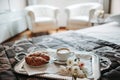 Tray with cappuccino, croissant and flowers on the bed