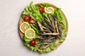 Tray with delicious fried anchovies, lemon slices, cherry tomatoes and lettuce leaves on white wooden table, top view Royalty Free Stock Photo