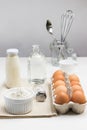 Tray of eggs and bowl of flour. Two bottles of milk and water. Metal whisk and spoon in glass jar Royalty Free Stock Photo