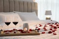 Tray with glasses of red wine, candles and rose petals on bed in room Royalty Free Stock Photo