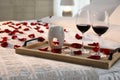 Tray with glasses of red wine, candles and rose petals on bed in room Royalty Free Stock Photo