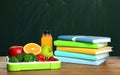 Tray with healthy food and notebooks on wooden table near green chalkboard. School lunch Royalty Free Stock Photo