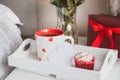Tray with a hot tea cup, cupcake, blank heart shaped card, gift box, and a bouquet of flowers in a vase on the bedside Royalty Free Stock Photo