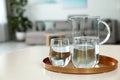 Tray with jug and glasses of water on white table in room. Refreshing drink