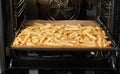 Tray with many crinkle fries in open oven Royalty Free Stock Photo