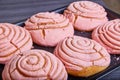 Tray of strawberry conchas Mexican sweet bread pastry baked good seashell swirl frosting pattern