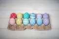 A tray with twelve colorful handmade Easter eggs lies on white wooden background, in the center.