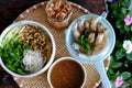 Tray of Vietnamese vegan food for lunch time, bowl of noodles with deep fried corn spring rolls and sliced cucumber, basil leaf,