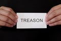 Treason crime case mug shot concept. Criminal hands holding paper placard with written word in dark black background.