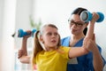 Strong resolute little girl raising hands with dumbbells