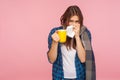 Treatment of seasonal flu. Sick girl wrapped in scarf blowing runny nose, sneezing in napkin and holding tea cup Royalty Free Stock Photo