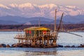 Trebuchet fishing hut at sunset against the Alps covered with snow, Marina di Pisa, Tuscany, Italy