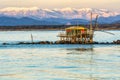 Trebuchet fishing hut at sunset against the Alps covered with snow, Marina di Pisa, Tuscany, Italy