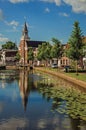 Tree-lined canal with bascule bridge, church, brick houses in street on the banks and sunny day at Weesp.
