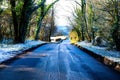 tree lined country lane going downhill, aspalt patches on the road, a layer of snow on each side covering the ground and trees Royalty Free Stock Photo