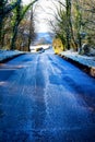 A tree lined country lane going downhill, aspalt patches on the Royalty Free Stock Photo