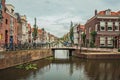 Tree-lined long canal with small bridge, brick houses on its bank and cloudy day at Gouda.