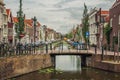 Tree-lined long canal with small bridge, brick houses on its bank and cloudy day at Gouda.