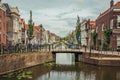 Tree-lined long canal with small bridge, brick houses on its bank and cloudy day at Gouda.