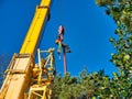 A tree surgeon wearing protective equipment and chain saw is suspended on the main hook block of a crane