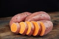 Tree sweet potatoes batatas, one of which is sliced, on the rustic wooden table with black background. Royalty Free Stock Photo