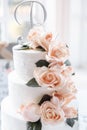 Tree-tired white wedding cake with natural peach roses and fake green leaves decorations Royalty Free Stock Photo